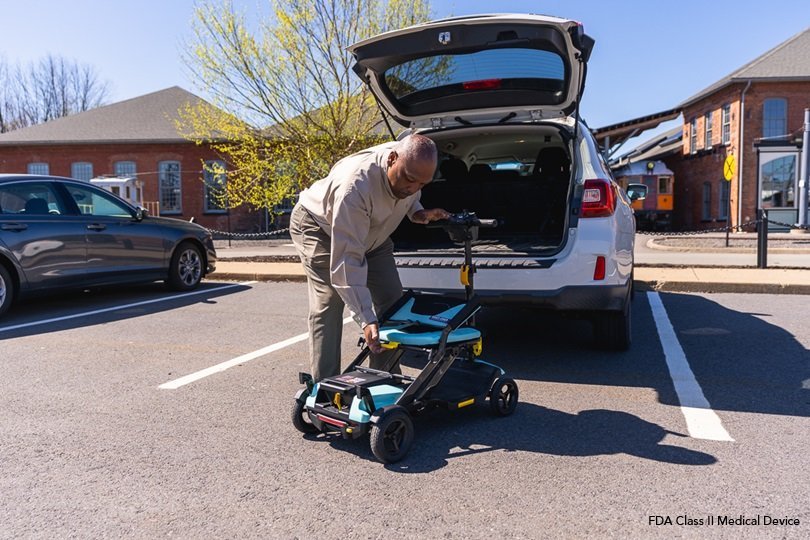 A compact foldable mobility scooter sitting on a sunny sidewalk in a city park.