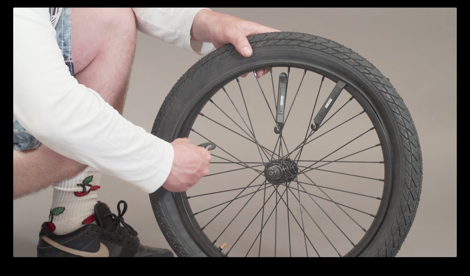 A mechanic replacing a worn BMX bike tire in a bright home garage.