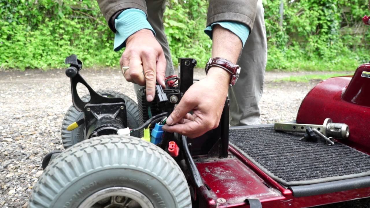 A person consulting a manual while performing mobility scooter battery maintenance at home.