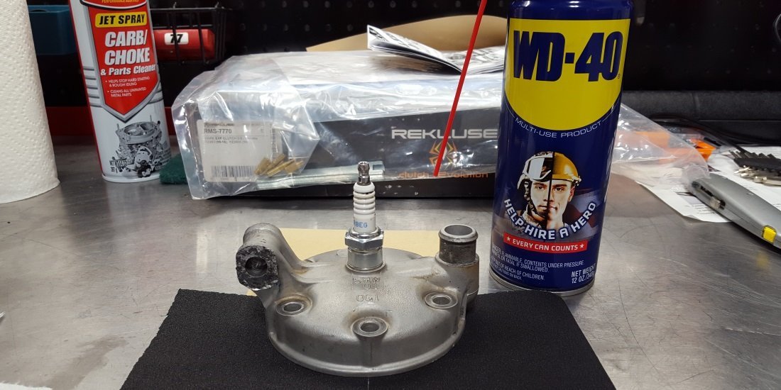 Cleaning supplies including brushes and solvent spray for a dirt bike engine.