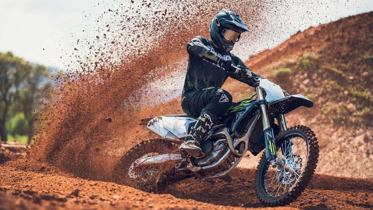 A gloved finger inspects the clean combustion dome of a dirt bike cylinder.