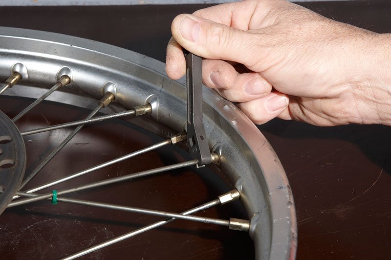 A gloved finger inspecting a clean and shiny dirt bike spoke.