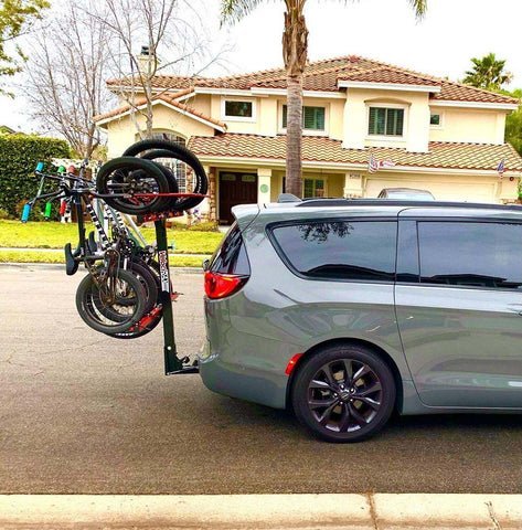 Hands testing the stability of a bike rack mounted to a minivan hitch.