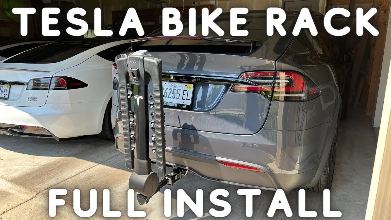 A modern electric vehicle with a hitch-mounted bike rack installed in a driveway.