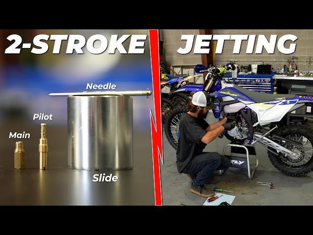 Cleaning a dirt bike carburetor jet with aerosol spray in a home workshop.