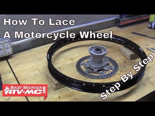 Hands adjusting the spoke tension on a dirt bike wheel using a wrench.