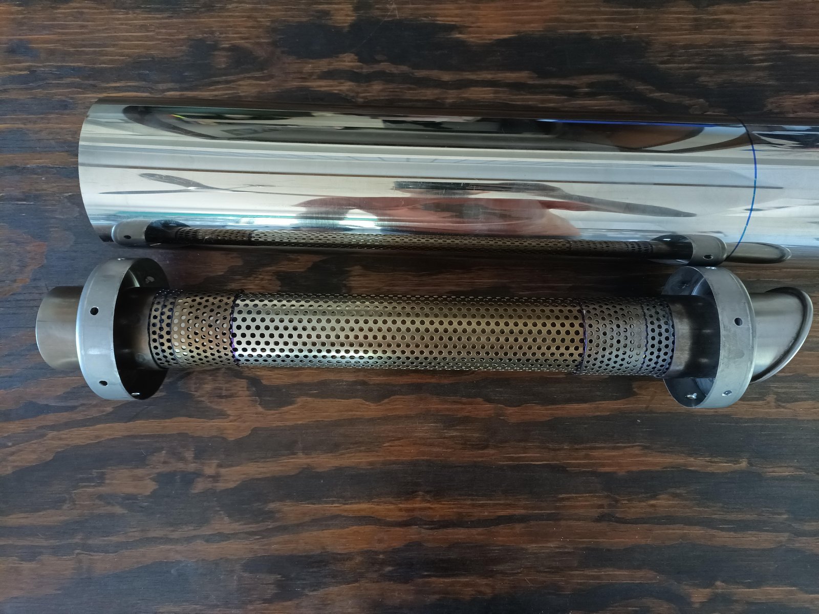 Raw materials for a dirt bike silencer organized on a workbench.