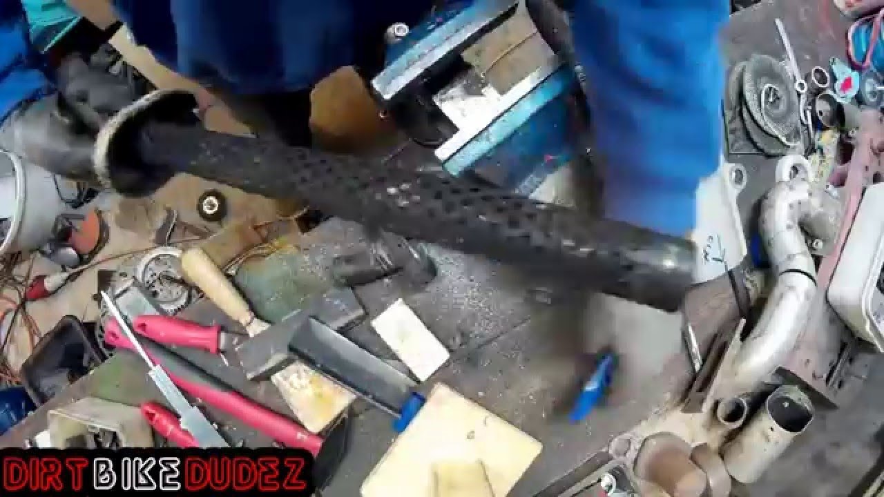 A mechanic checks the structural integrity of a dirt bike silencer.