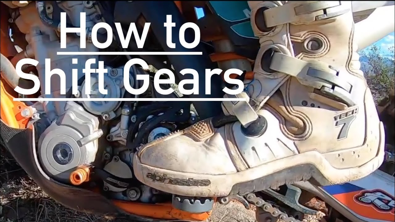A rider's boot pressing the shift pedal on a two-stroke dirt bike.